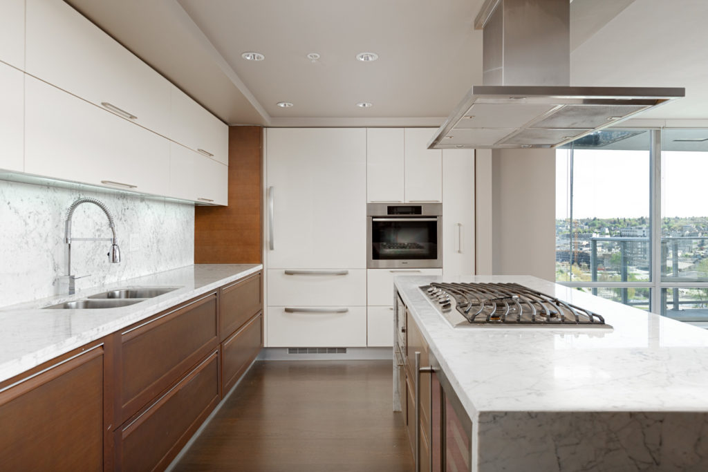 Kitchen with stainless steel appliances and marble counter top inside luxury Vancouver condo.