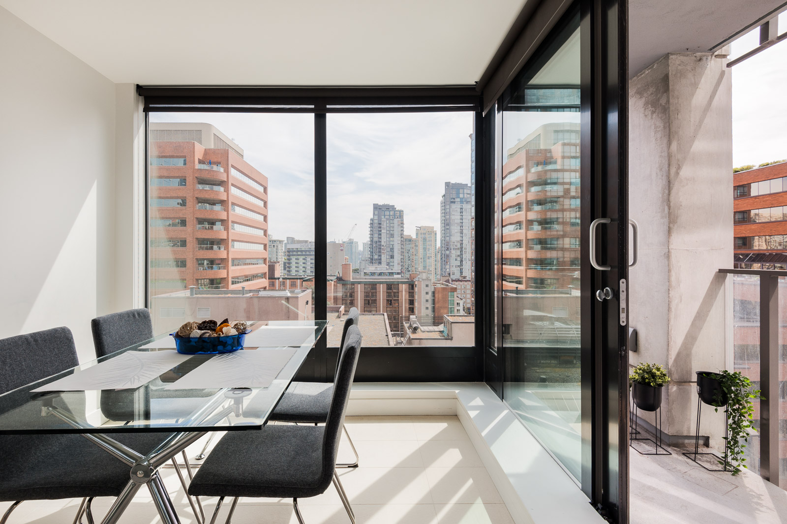 Glass dining table with four black chairs overlooking Vancouver from luxury rental.