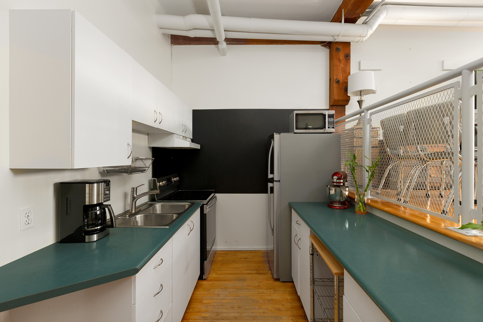 kitchen with dark grey countertops and hardwood floors and ventilation pipes on ceiling in rental condo