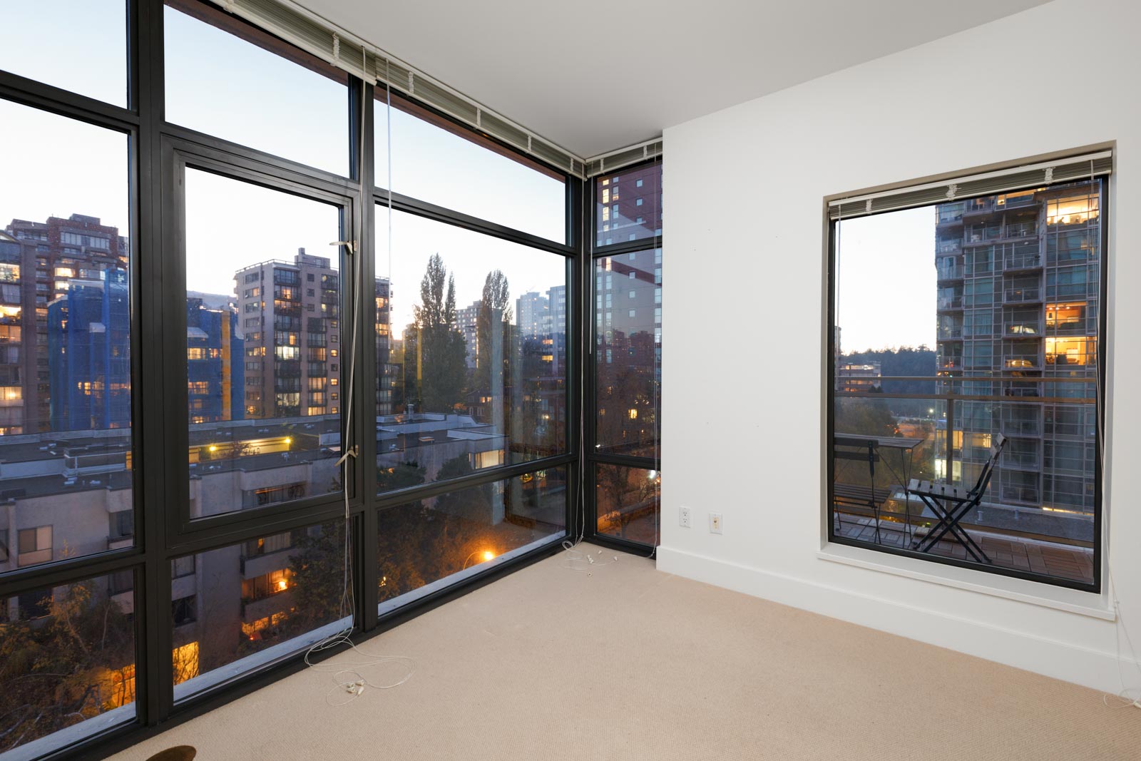 corner of empty condo bedroom with floor to ceiling windows on left and white wall and hung mirror on right