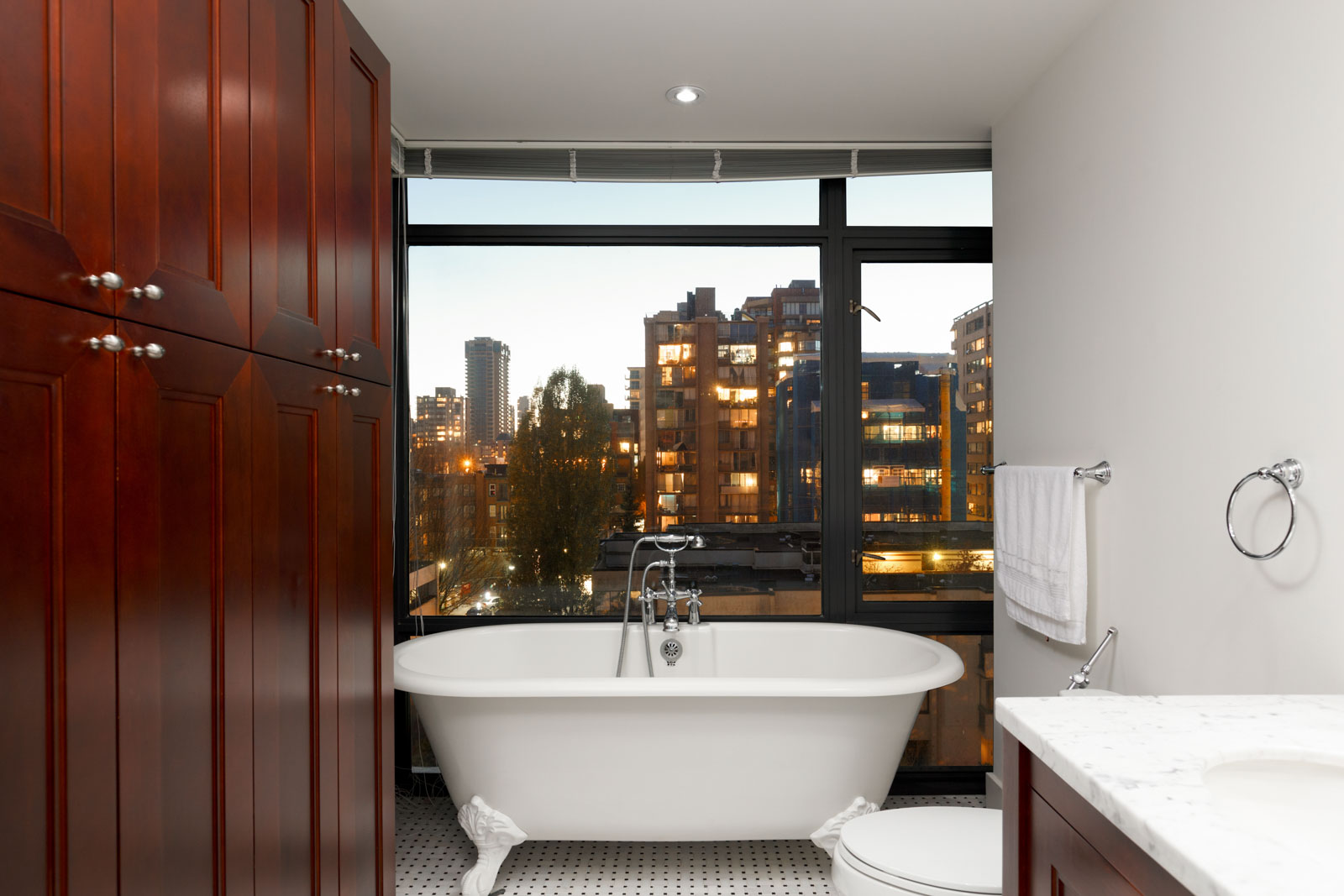 standalone bath tub against the window of bathroom with wood cabinets and walls on left in lumiere condo in west end vancouver