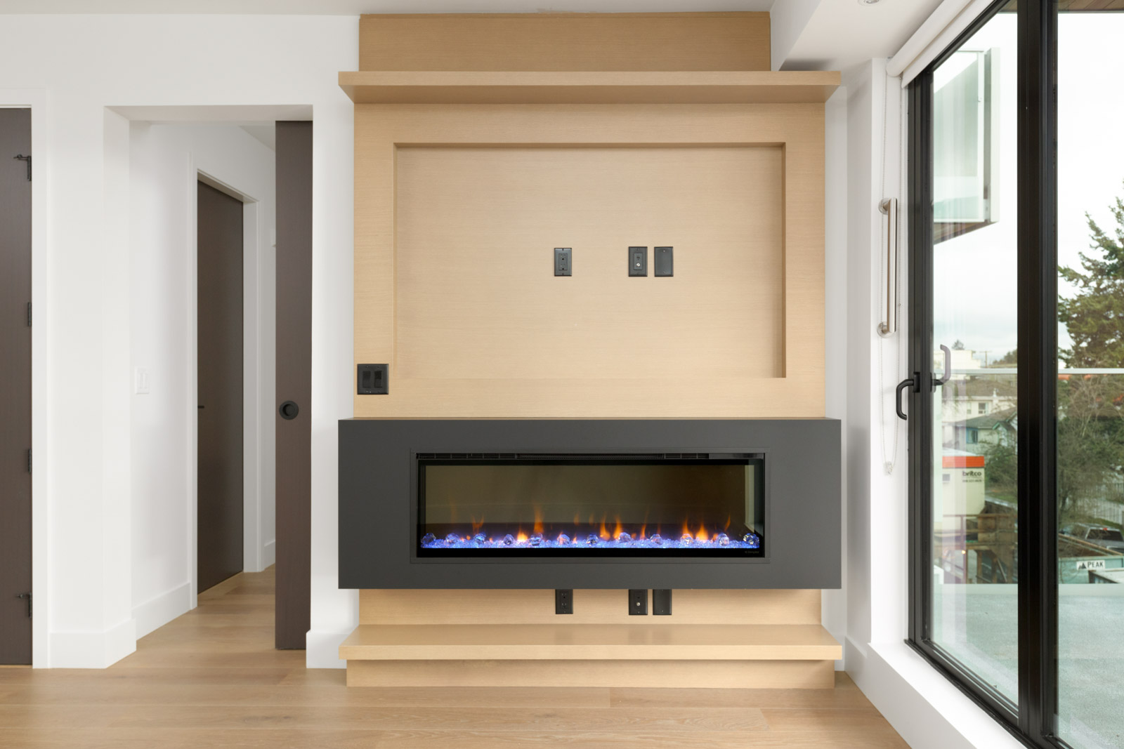 black fireplace with wooden wall in condo living room with window on right in little mountain mount pleasant area of vancouver