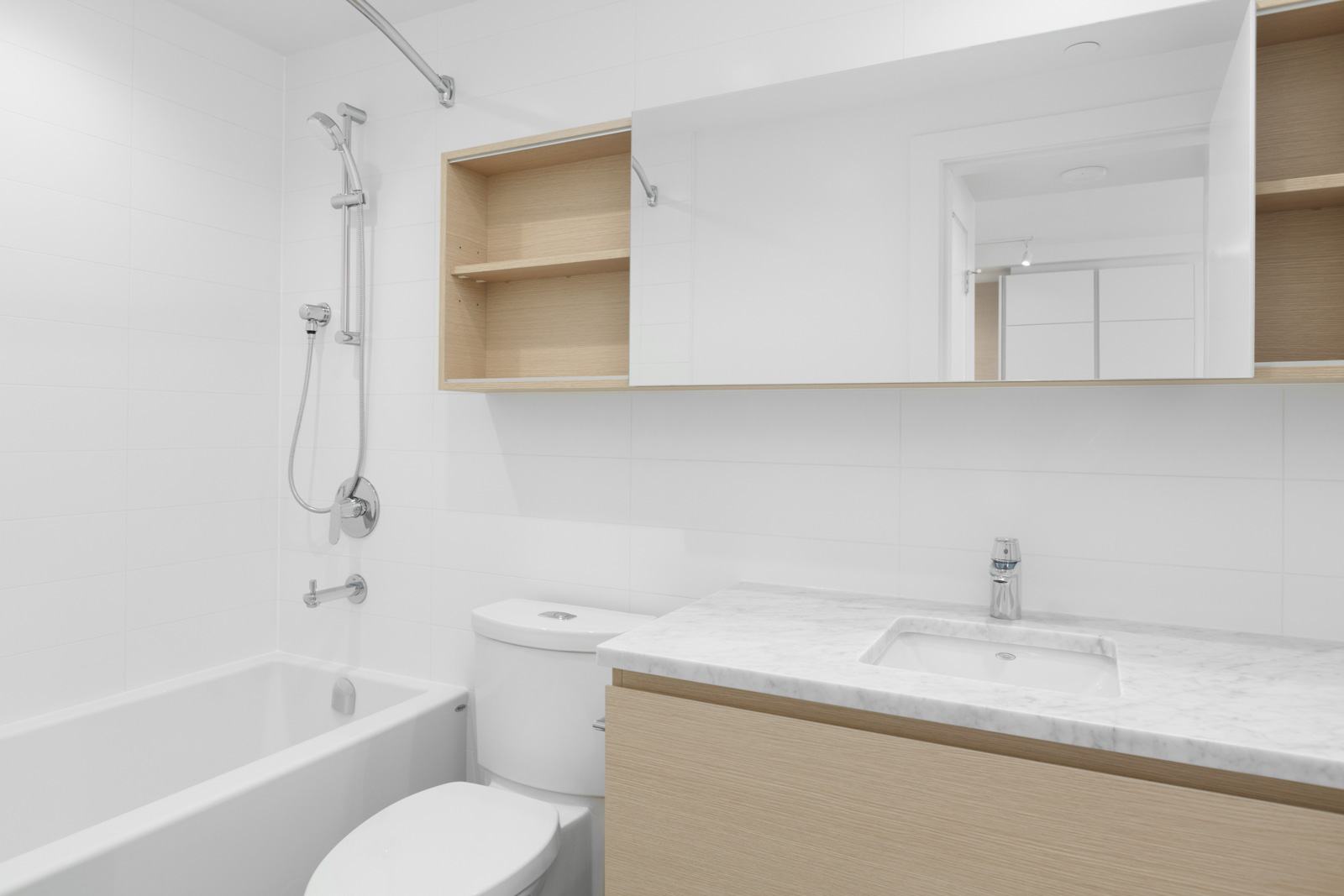 condo bathroom with vanity and sink on right and toilet in middle with shelving above and shower on left
