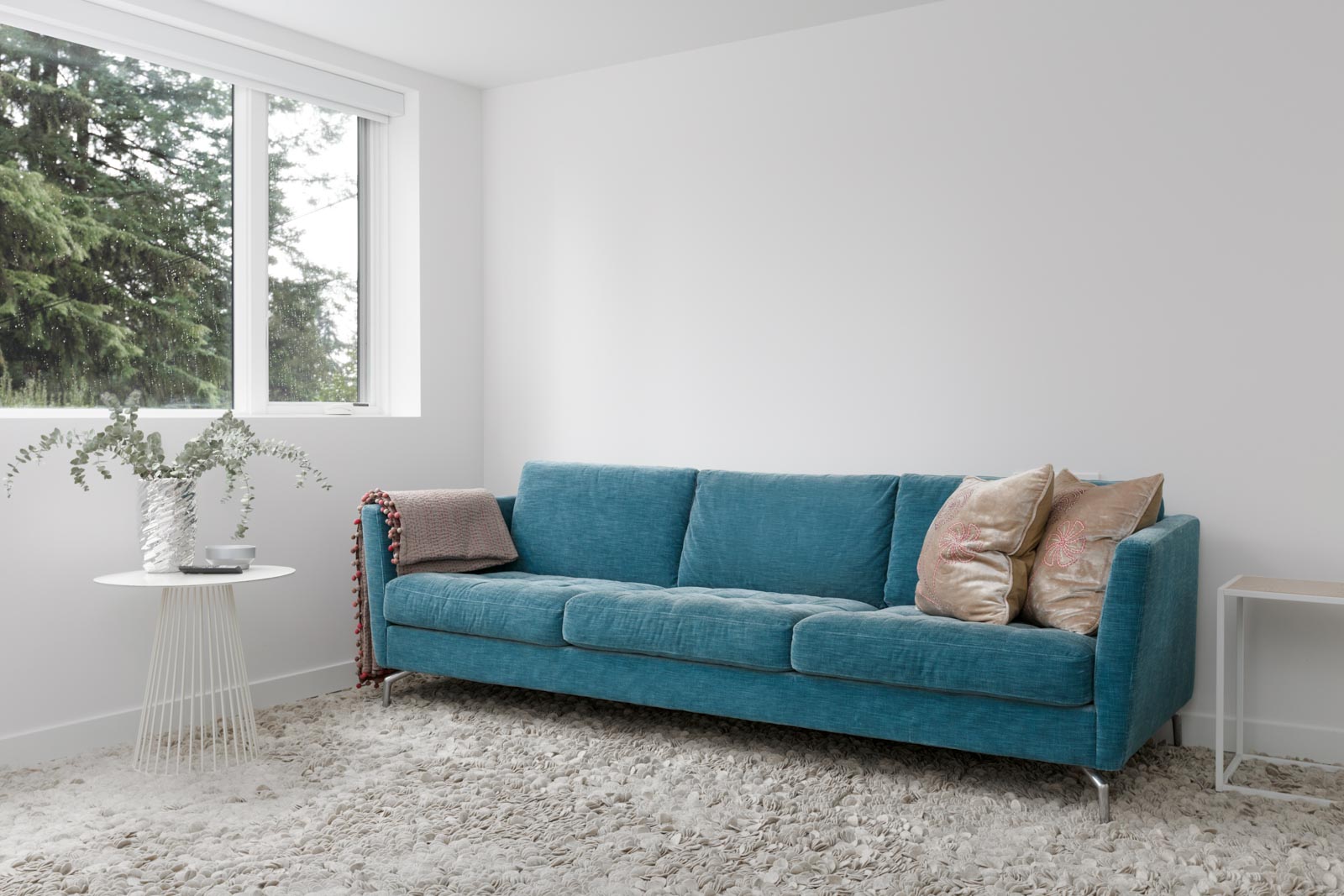 blue couch and grey rug in living room of basement rental suite in modern designed house with white walls and window on left and exposed concrete floors