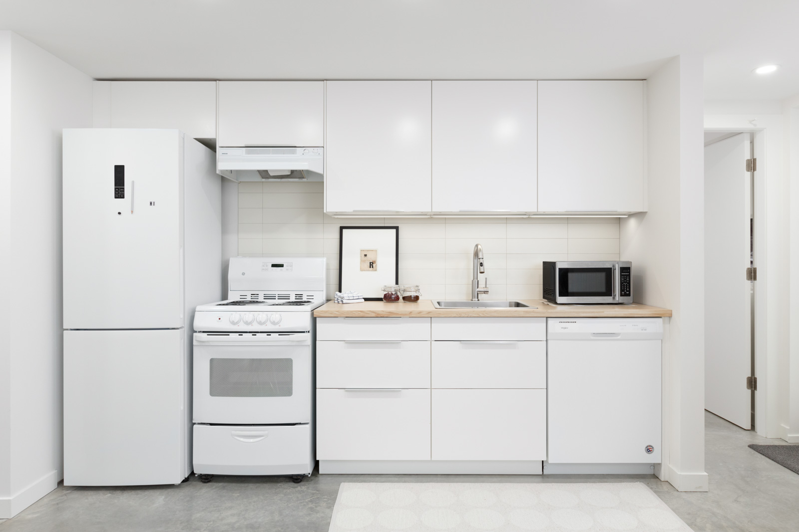white kitchen wall with cabinets of basement rental suite in north vancouver with stove and oven on left and small black microwave on counter on right