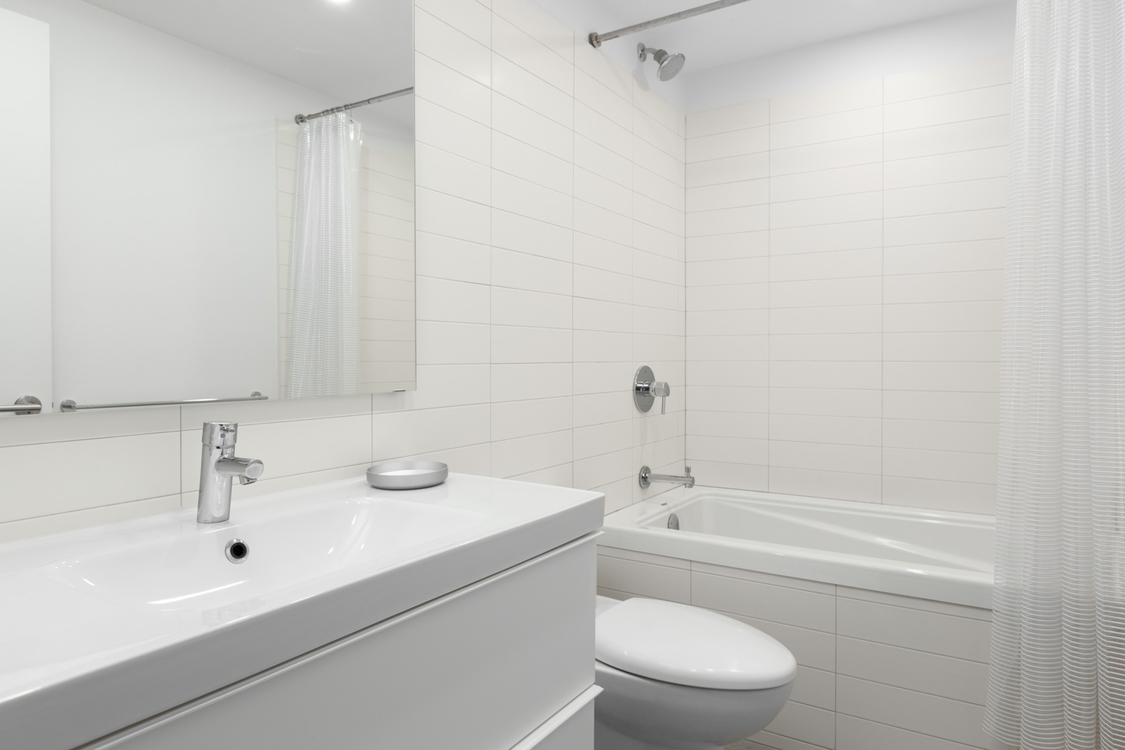 white bathroom in rental suite of house with vanity sink and mirror on left and toilet in middle and bathtub with shower on right with white tiles
