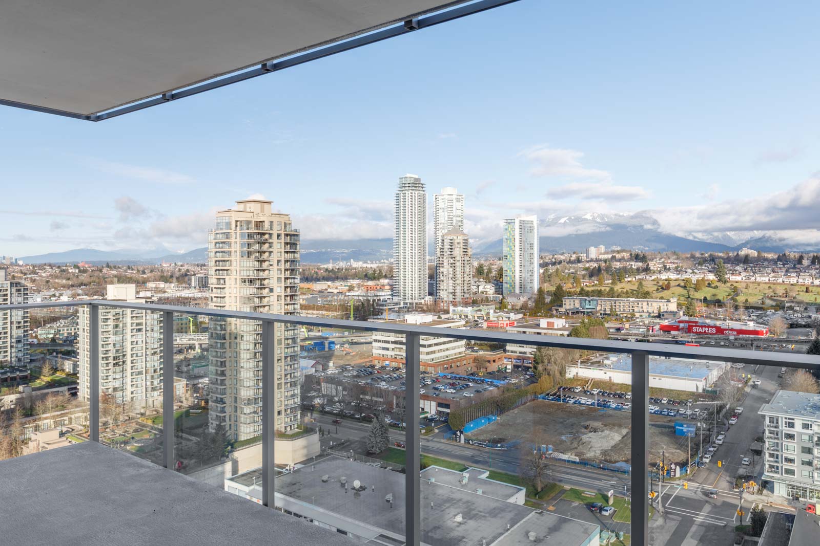 View from a high-rise balcony overlooking city buildings, with mountains visible in the distance under a partly cloudy sky.