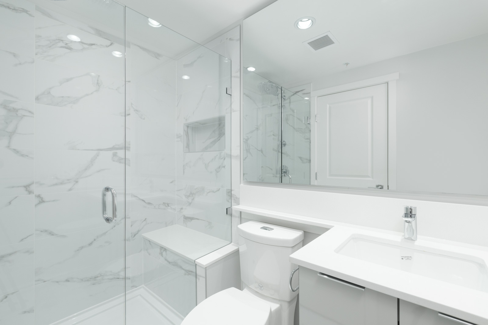 Modern bathroom with a glass-enclosed shower, white toilet, white vanity with sink, large mirror, and marble-patterned walls.