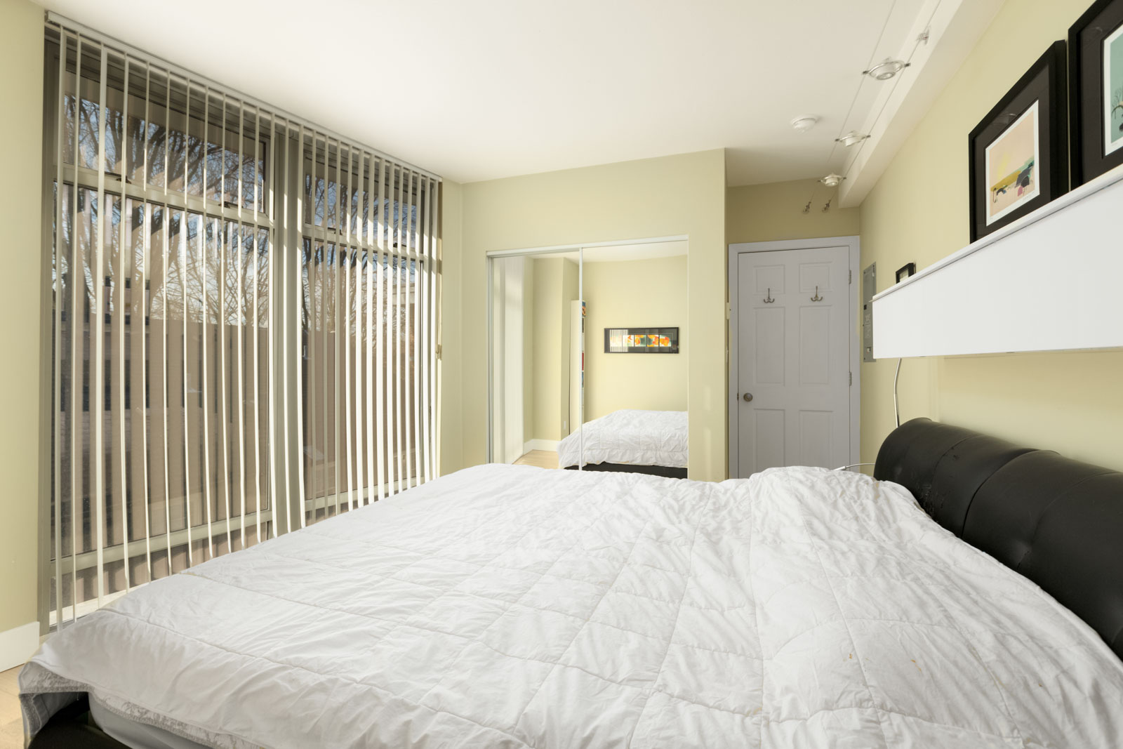 bedroom of rental condo in vancouver with bed with white sheets in foreground and mirrored closed closet and closed door in background