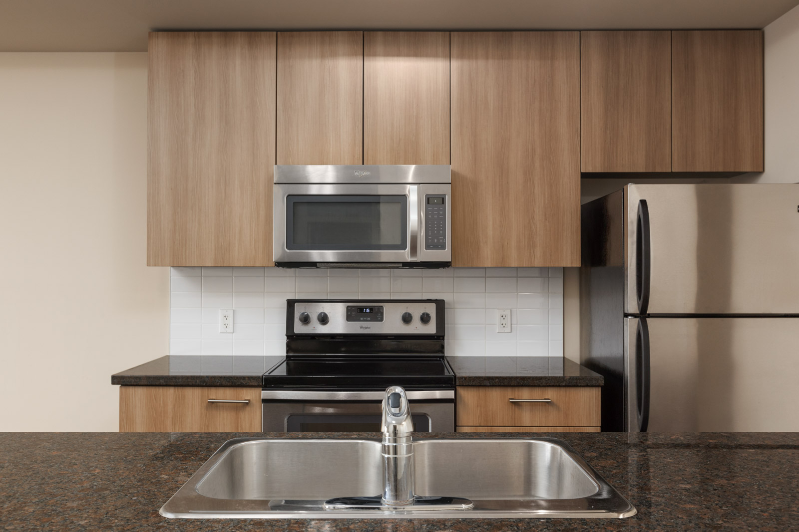 kitchen with island microwave oven and stove top and sink in island in the foreground in a rental condo in richmond at remy on stolberg managed by birds nest properties