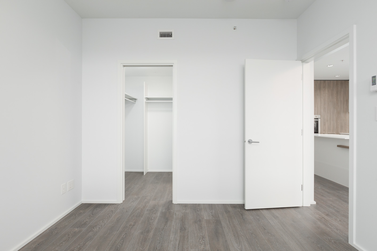 empty bedroom with open closet doors and open door on right and hardwood floors in brentwood tower one condo building