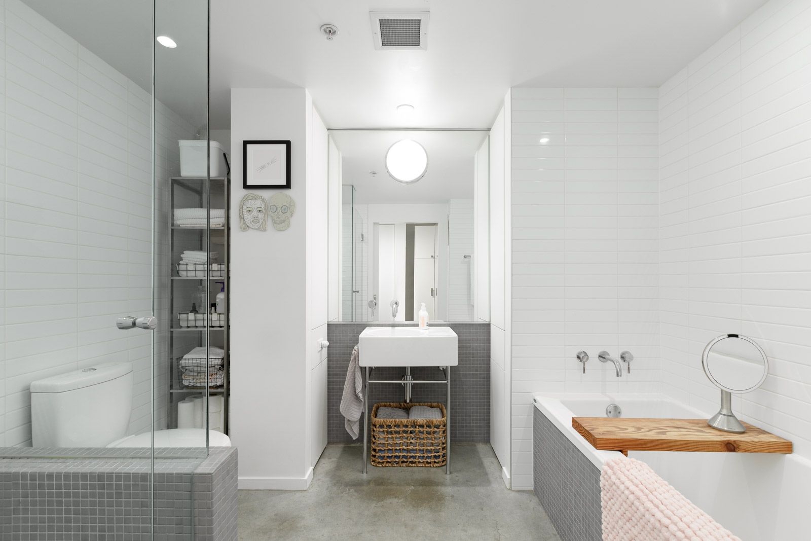 sleek bathroom with modern light fixtures and appliances, with hidden storage to the far left and bathtub to the far right in a rental condo provided by Birds Nest Properties in Vancouver