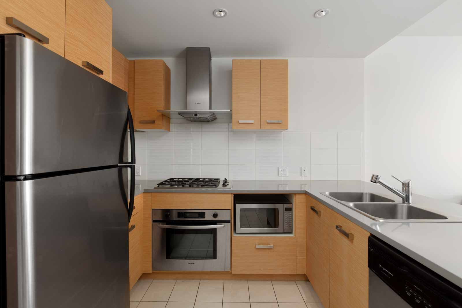 Open kitchen with high-end stainless steel appliances including oven, stove, refrigerator, and sink, with plenty of counter and storage space in a rental condo in Richmond offered by Birds Nest Properties