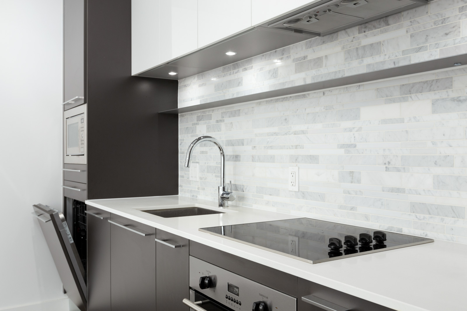 Sleek kitchen with a tiled backsplash and high-end appliances such as a dishwasher, microwave, stovetop on quartz countertops in a rental condo in Vancouver offered by Birds Nest Properties.