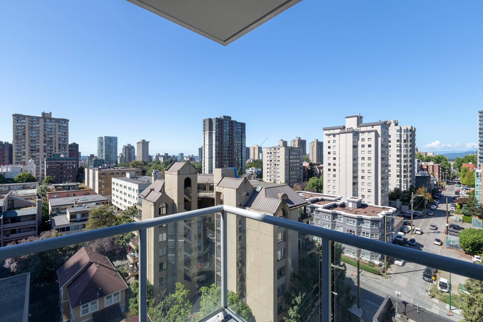 View from a balcony showing a cityscape with several mid-rise and high-rise apartment buildings under a clear blue sky.