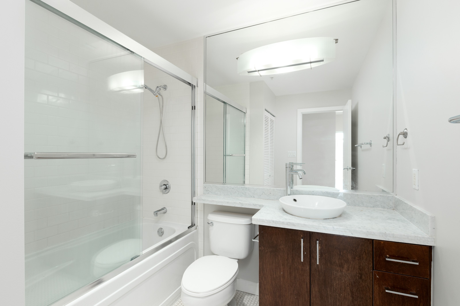 Modern bathroom with a glass-enclosed shower and bathtub, a vanity with a vessel sink, large mirror, and white and dark wood accents.