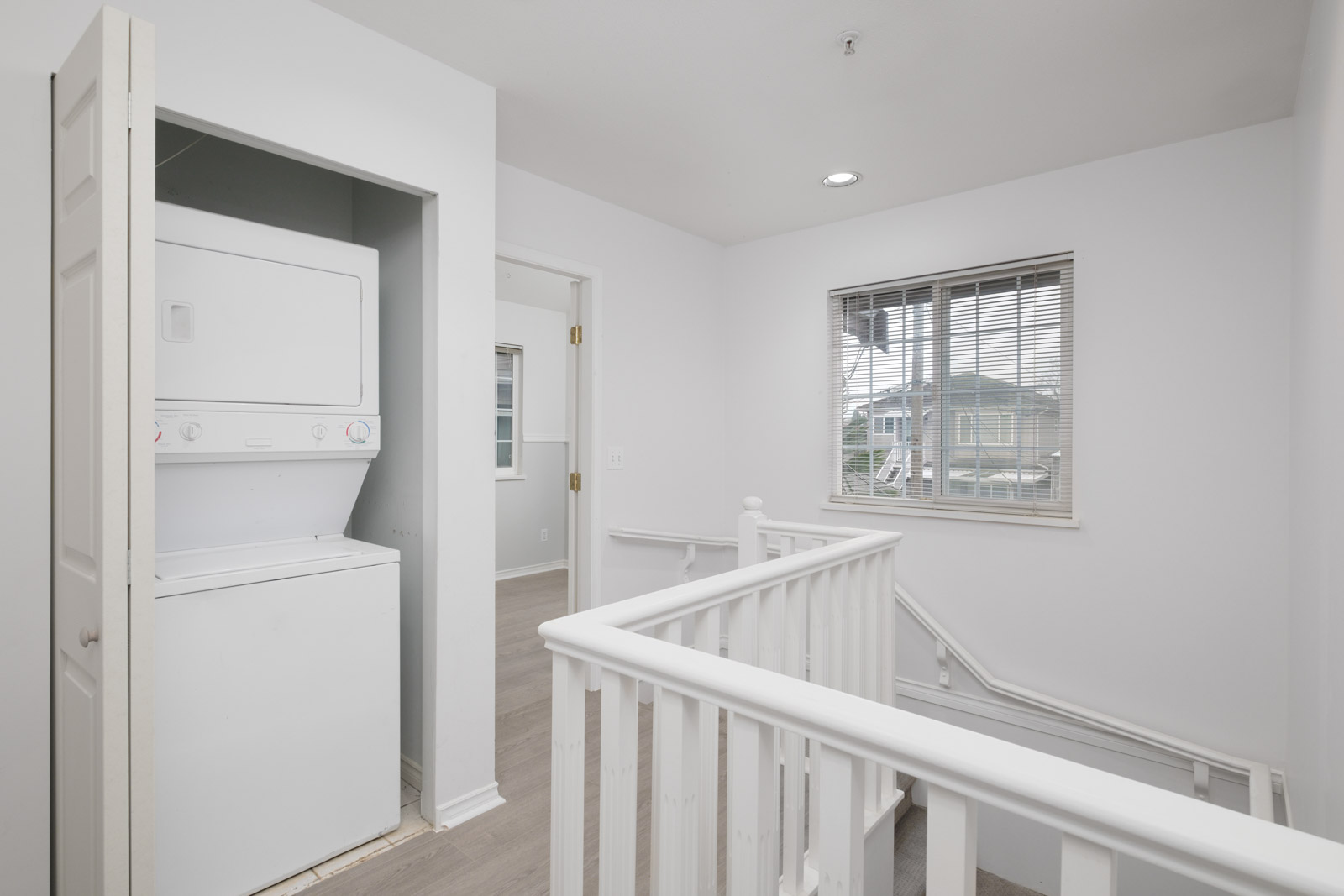 room with stacked white washer and dryer in open closet on left and beside railing to stairs in rental house in east vancouver