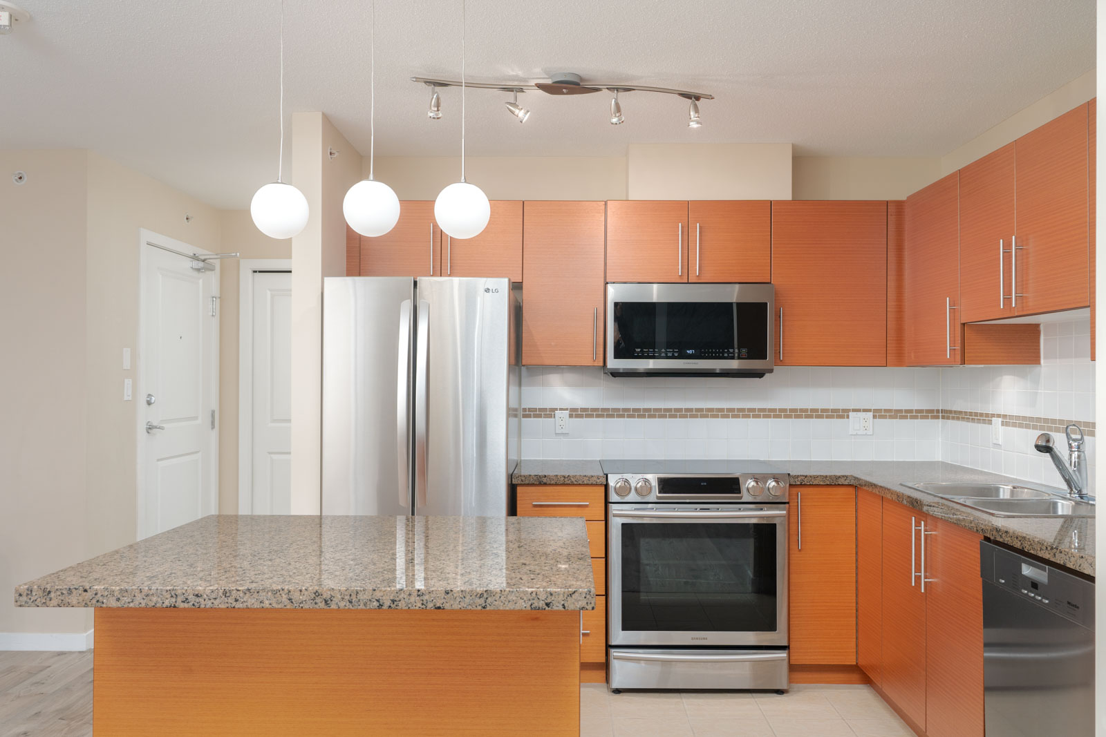 Modern kitchen with wood cabinets, granite countertops, stainless steel appliances, island, and three globe pendant lights.