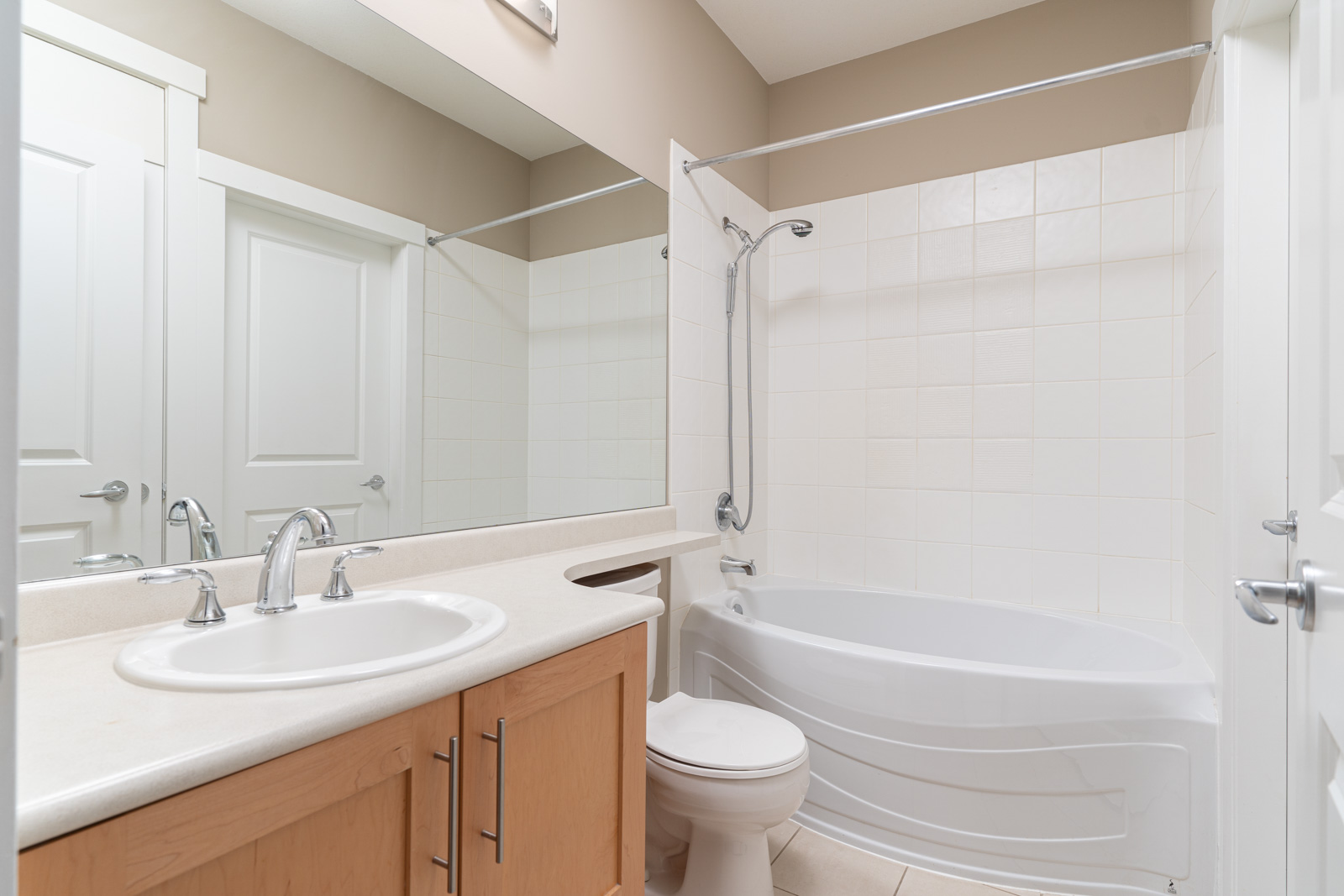Modern bathroom with a white sink, a toilet, a bathtub with a showerhead, a large mirror, and light wood cabinetry.