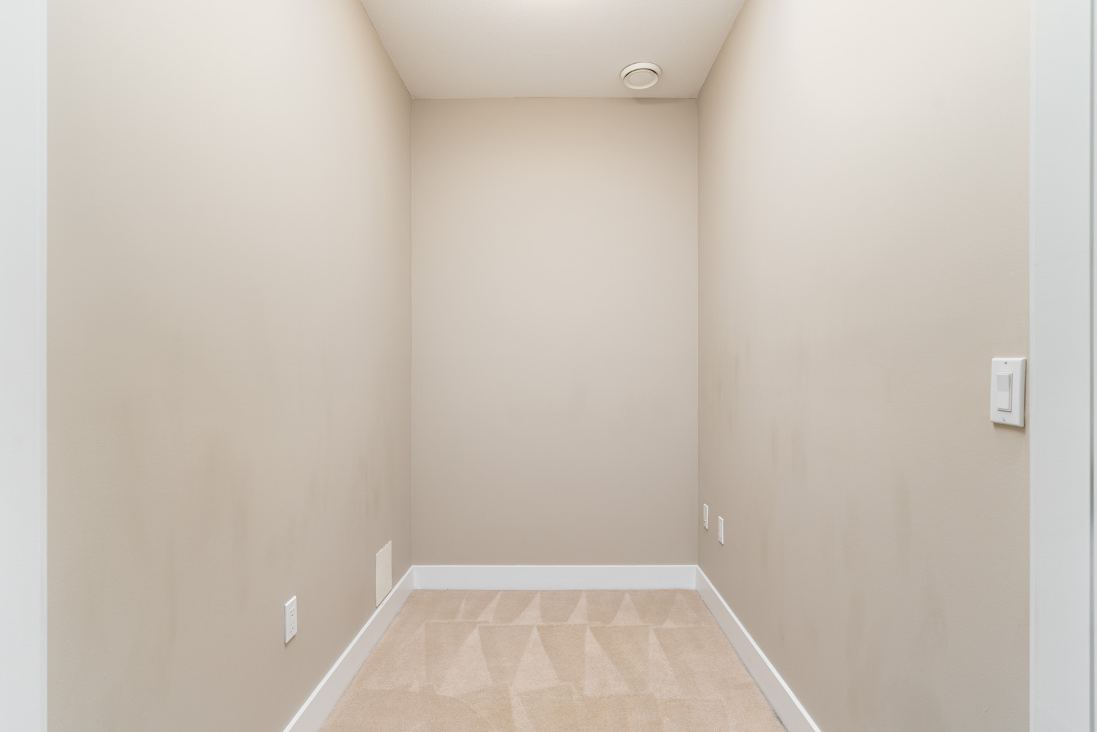 Empty beige-walled alcove with clean carpet, ceiling vent, and several electrical outlets, viewed from the entrance.