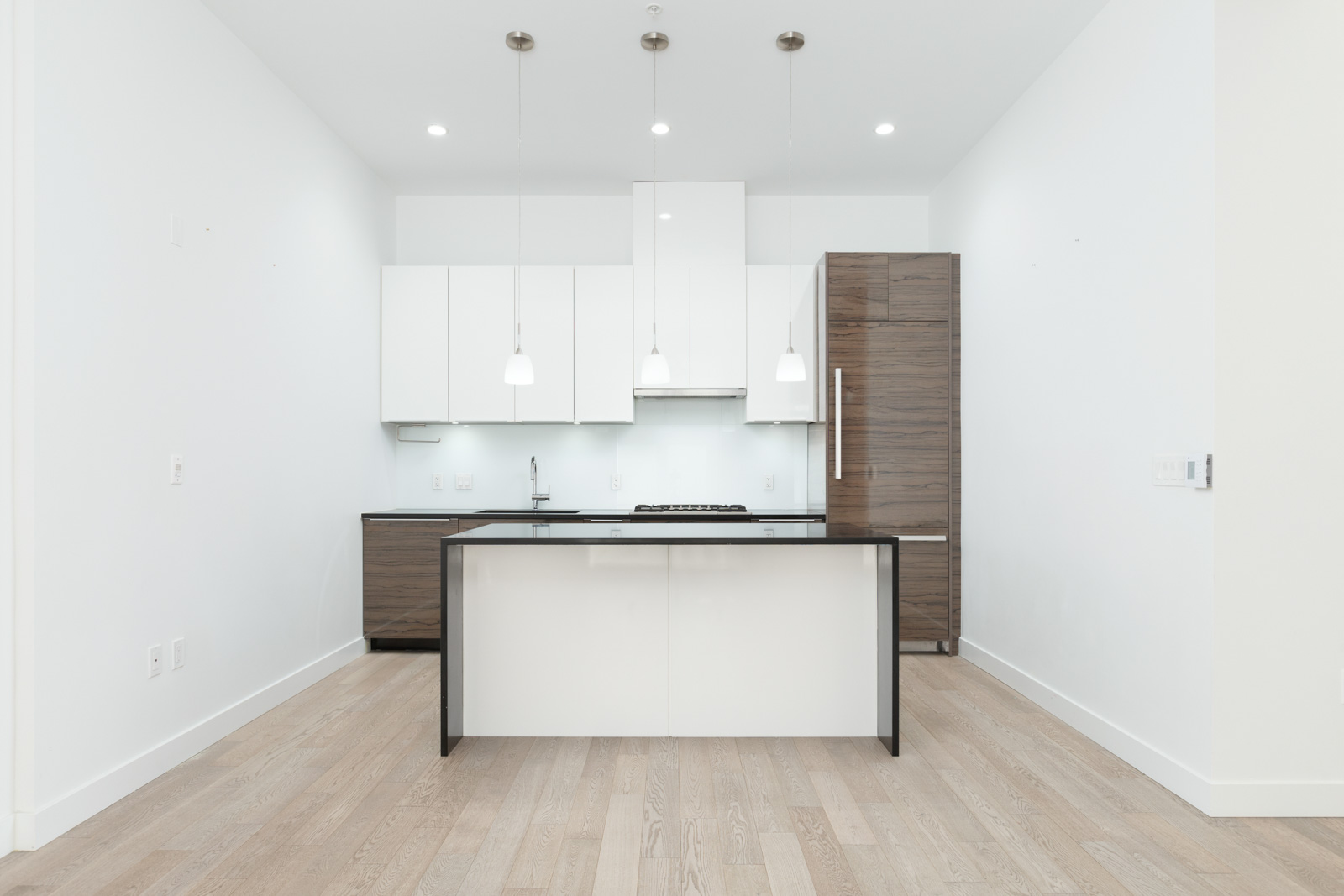 Modern, minimalist kitchen with white cabinets, wooden accents, a central island, pendant lights, and light wood flooring.