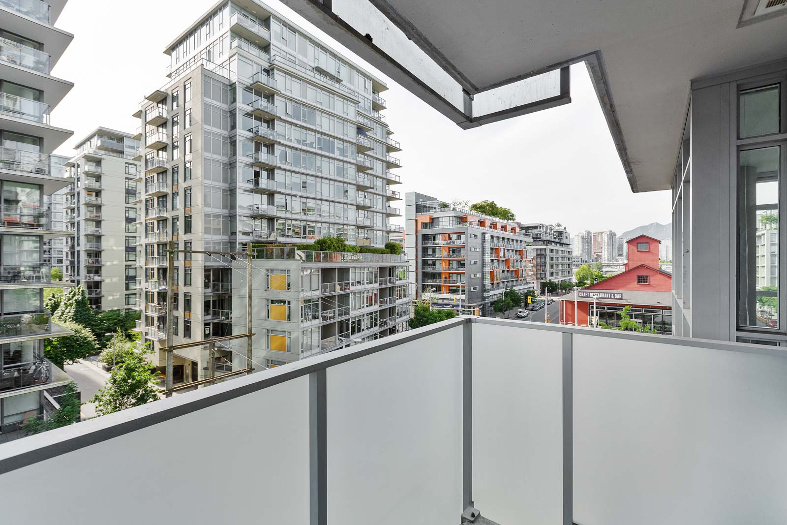 View from a balcony overlooking modern apartment buildings, with a red building visible among high-rises and trees in an urban setting.