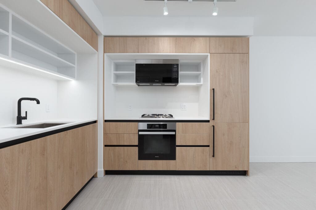 Modern kitchen with light wood cabinets, black appliances, a built-in oven, microwave, gas cooktop, and a matte black faucet on a white countertop.
