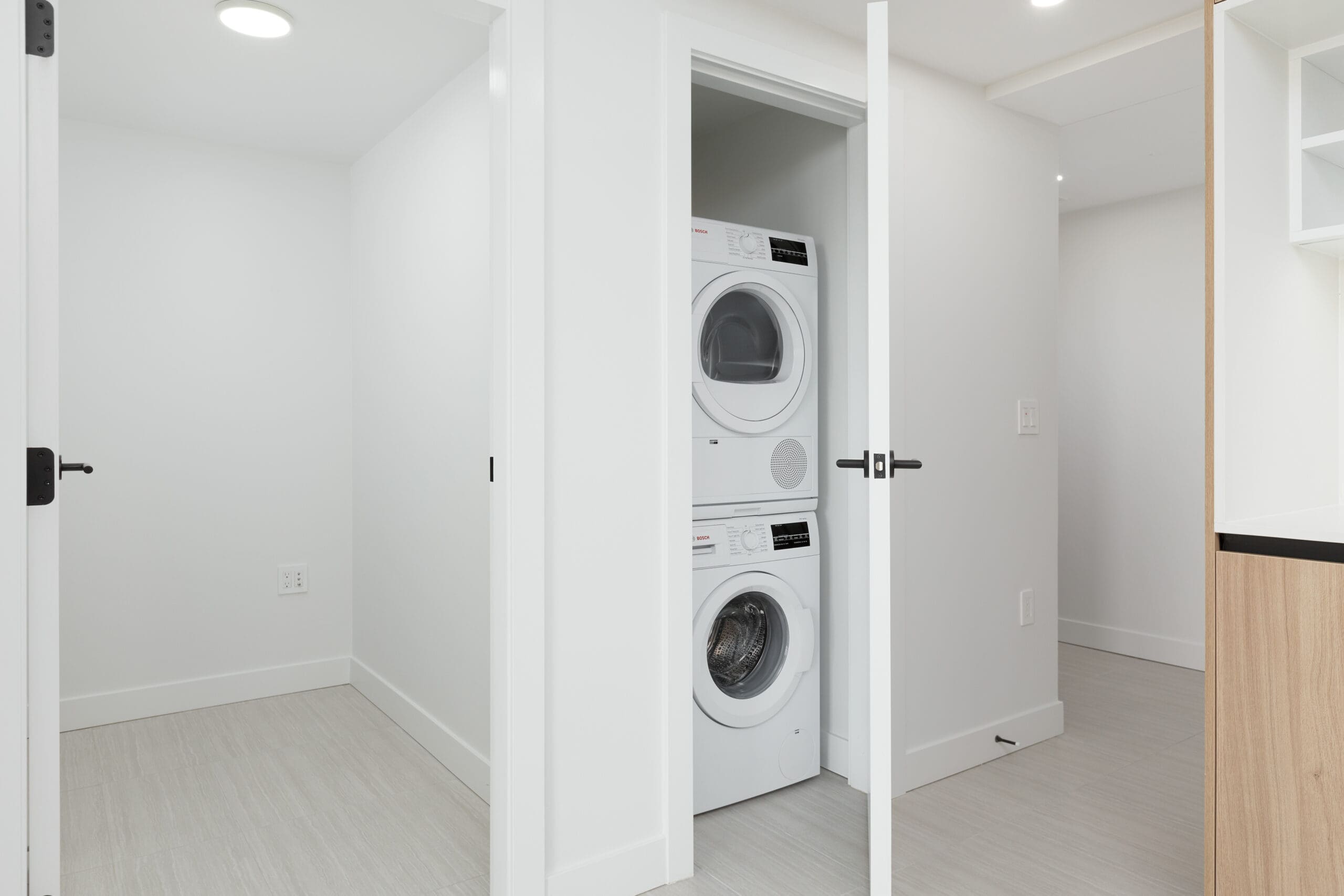 A small laundry closet with a stacked washer and dryer unit, white walls, and light-colored flooring in a modern home.