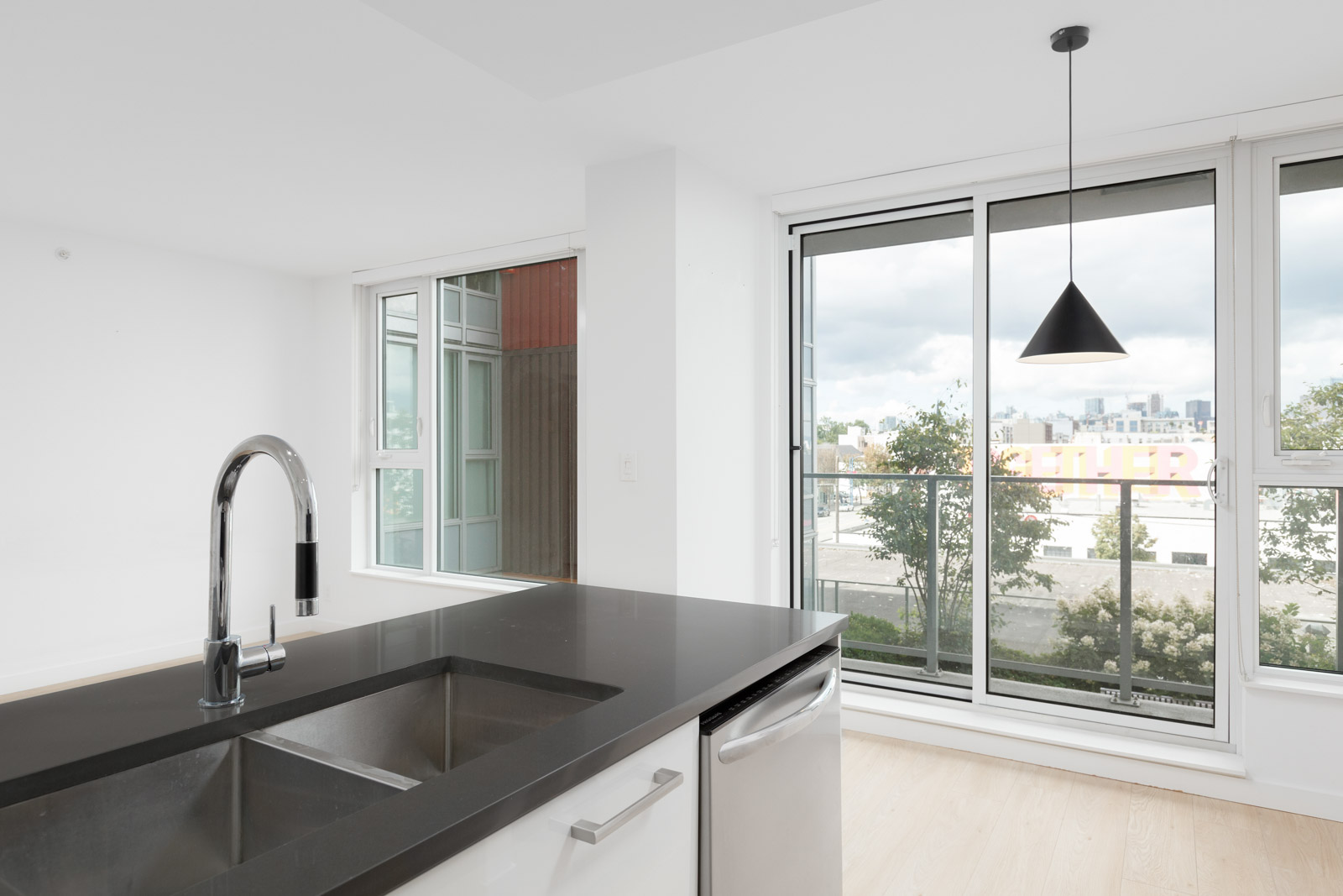 Modern kitchen with a black countertop island, stainless steel sink, and faucet. Large windows and a sliding glass door provide natural light and a city view.