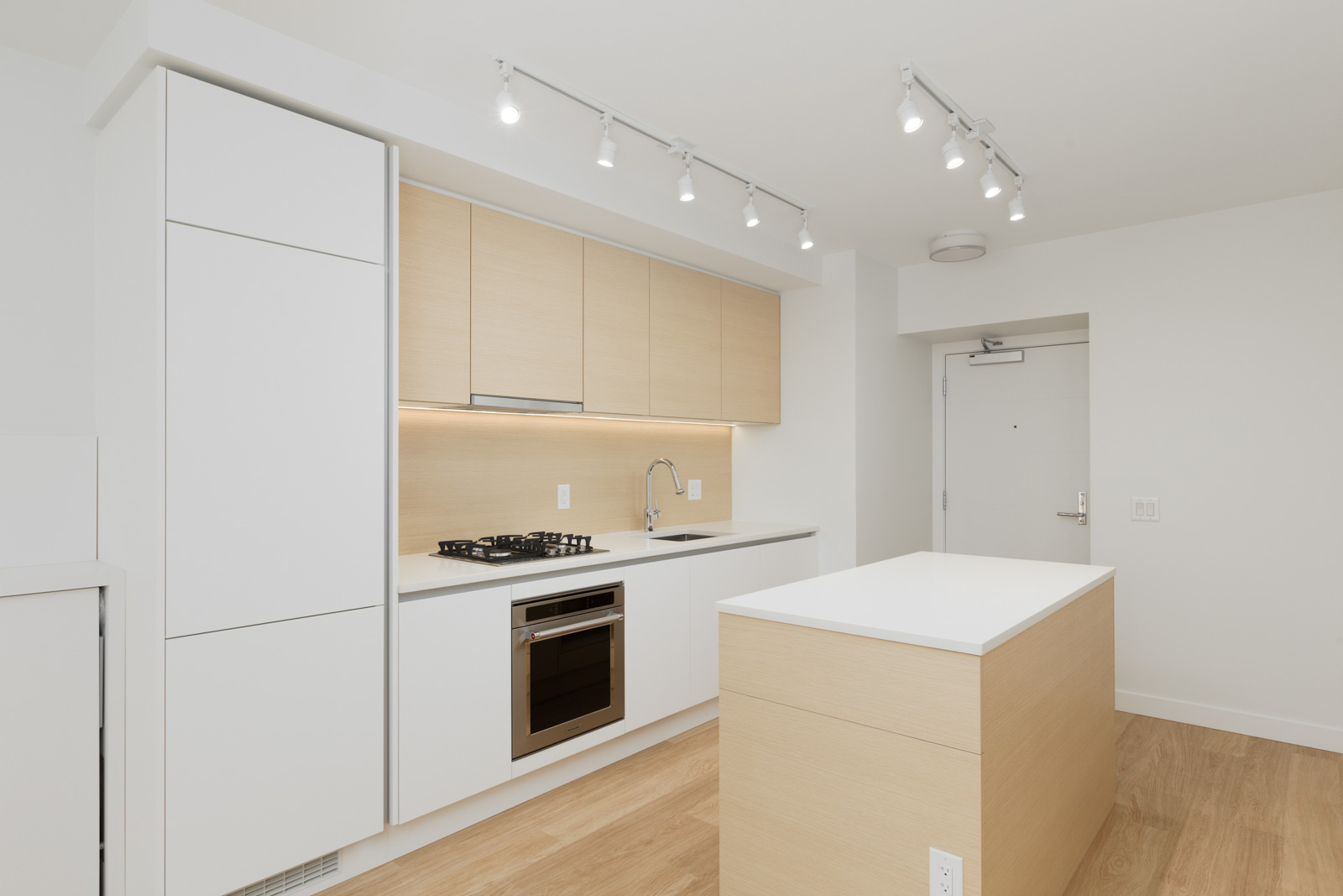 Modern kitchen with light wood cabinets, white countertops, a built-in oven, gas cooktop, island, and track lighting, all in a minimalist design.