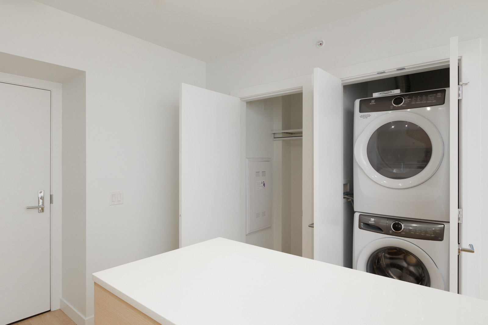 A modern laundry closet with a stacked washer and dryer unit behind open doors in a bright, minimalist room.