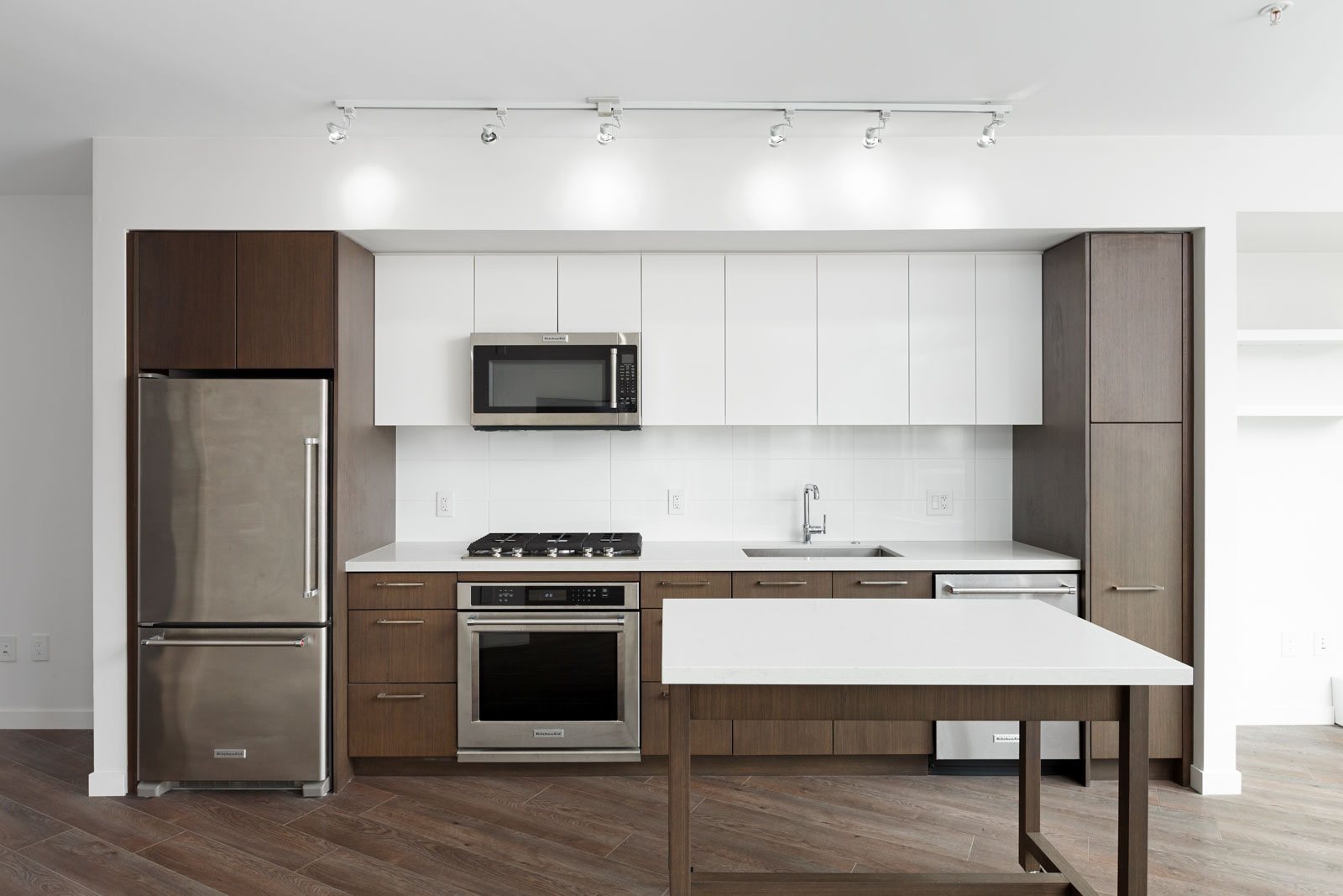 Modern kitchen with stainless steel appliances, white upper cabinets, brown lower cabinets, white countertop, and a central island.