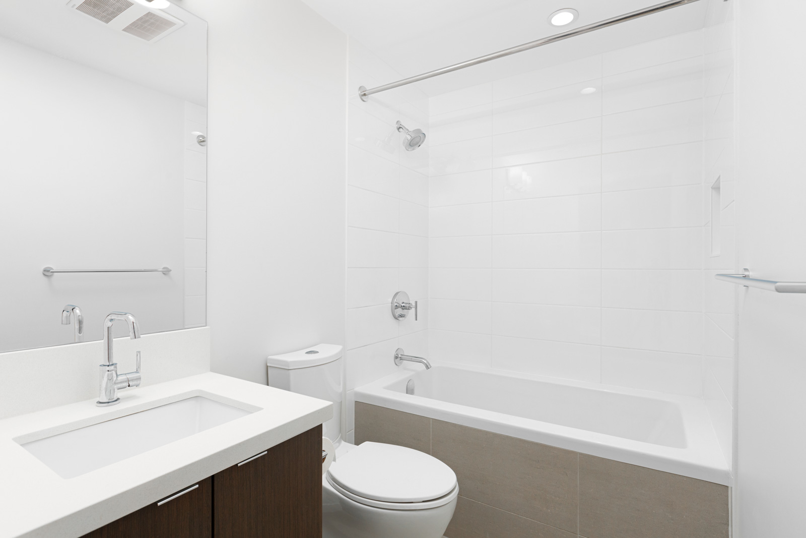 Modern bathroom with a white bathtub, shower, toilet, and sink vanity with a mirror; clean, minimalist design with neutral tones.