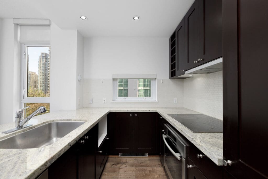 Modern kitchen with dark cabinets, light granite countertops, stainless steel sink, electric cooktop, and two windows providing natural light.