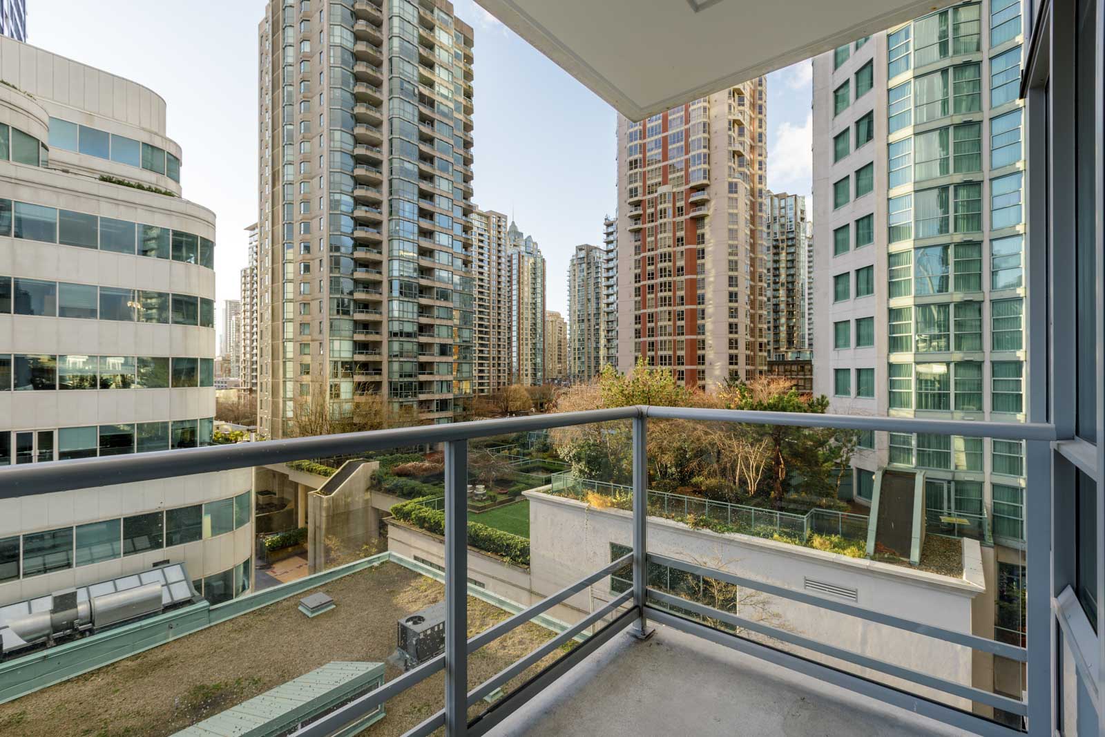 View from a balcony overlooking a modern cityscape with high-rise residential and office buildings, landscaped courtyard, and clear sky.