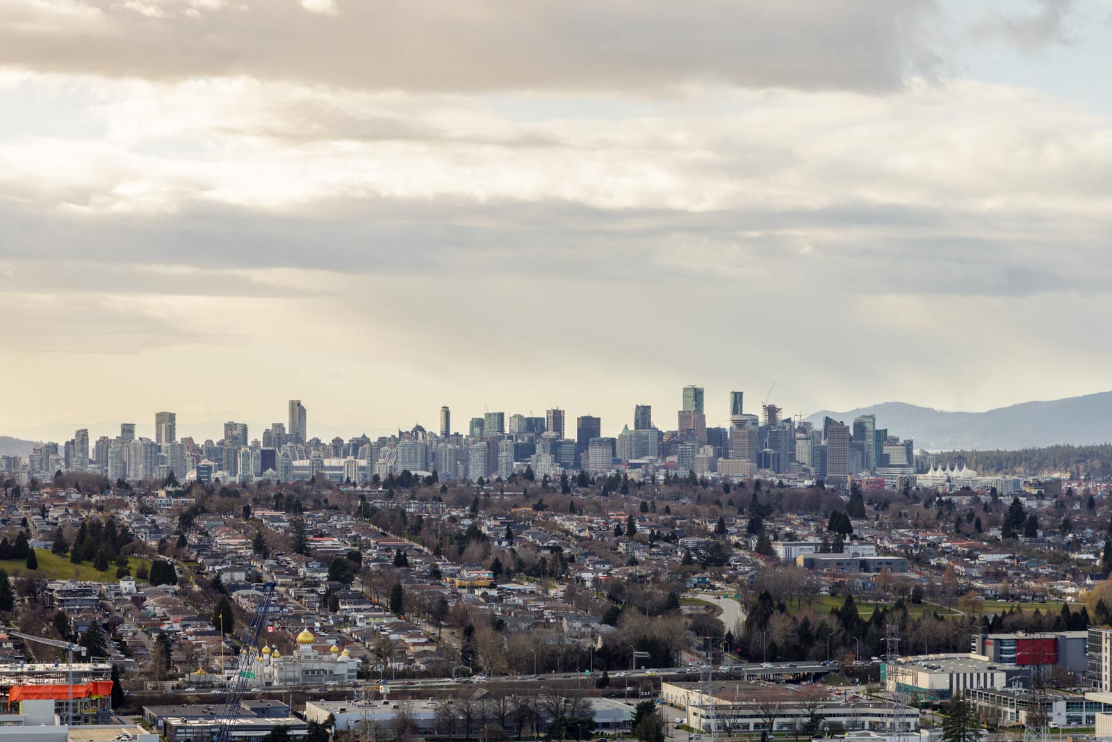 A city skyline with modern high-rise buildings under a cloudy sky, with residential neighborhoods and trees in the foreground.