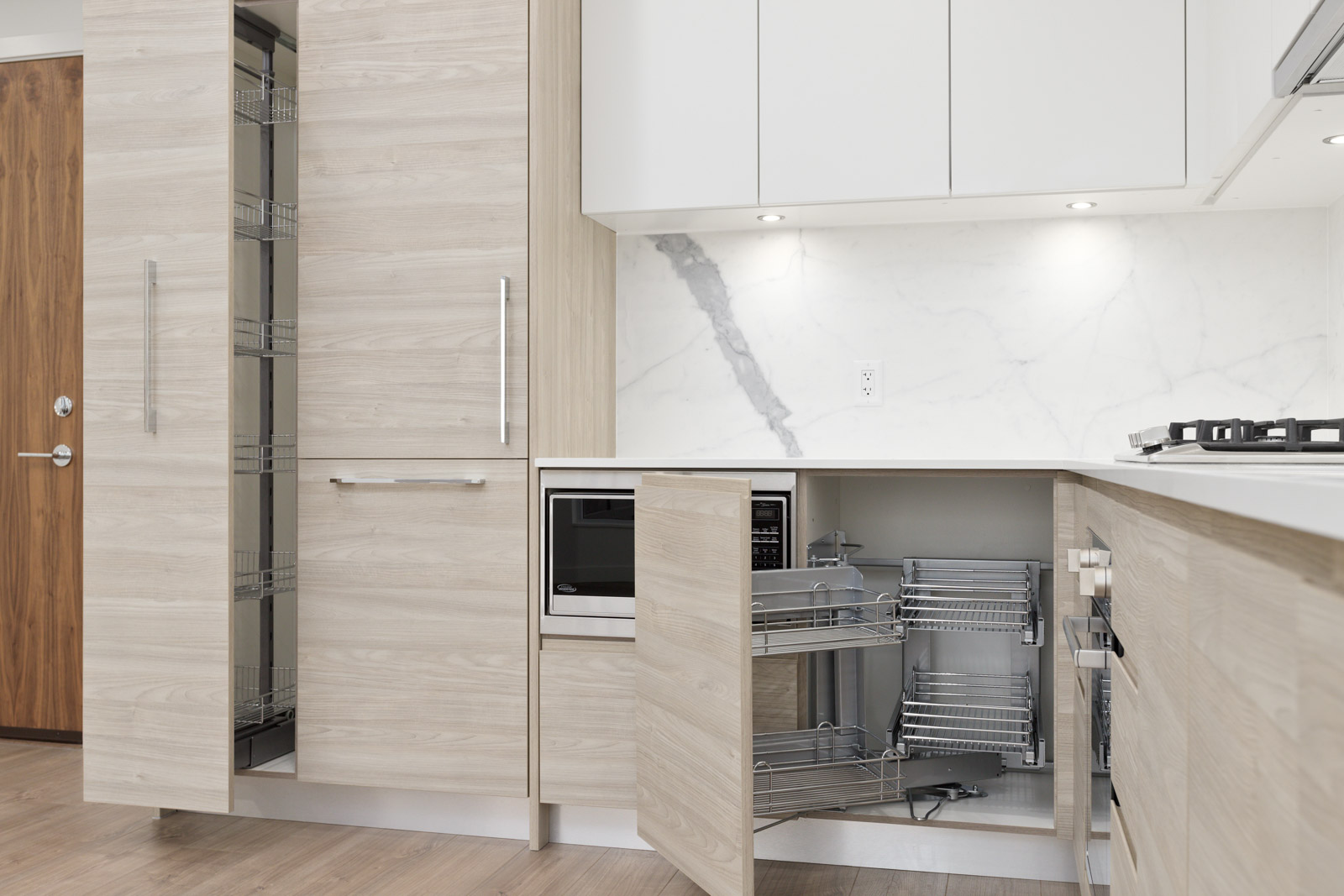 Modern kitchen with light wood cabinets, a pull-out pantry, a built-in microwave, and open corner cabinet shelves, featuring a white marble backsplash.