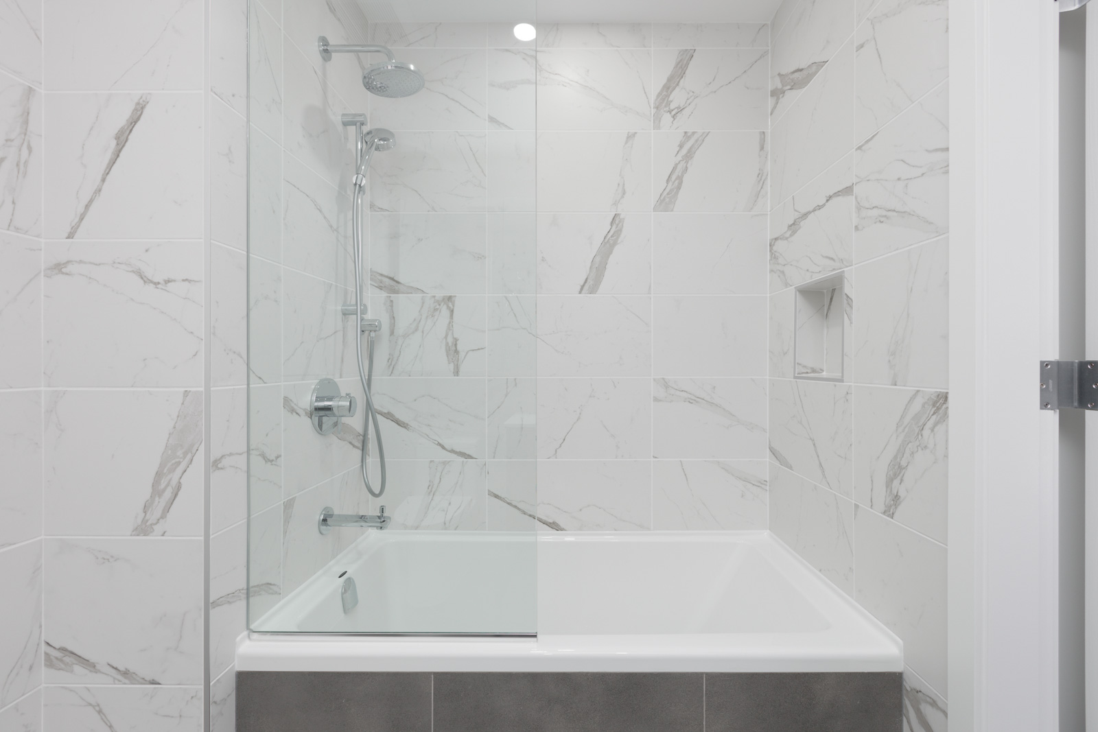 marble style bathroom walls with glass divider and deep soaker tub