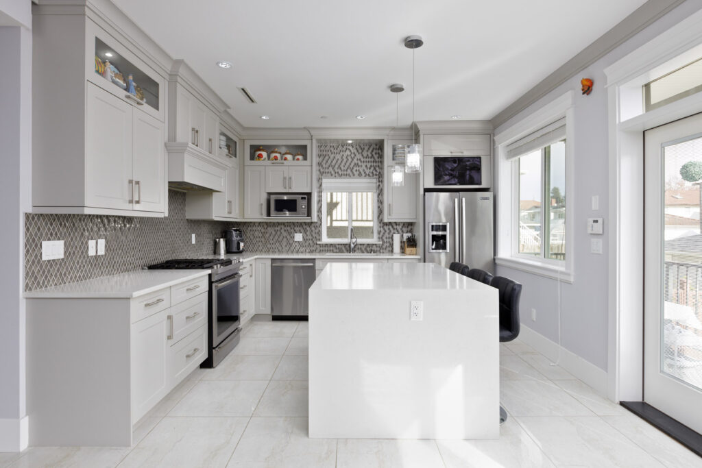 large kitchen with white island and stainless steel appliances. White cabinets with tiled light and dark backsplash