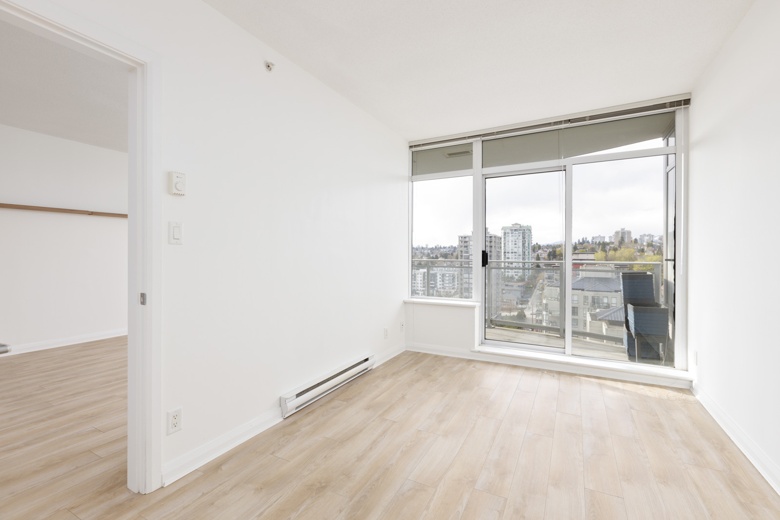 bedroom with white wall and light wood flooring. large floor to ceiling windows with balcony door