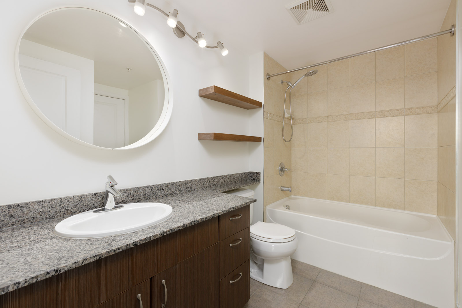 washroom with round mirror, dark cabinets, tiled shower area