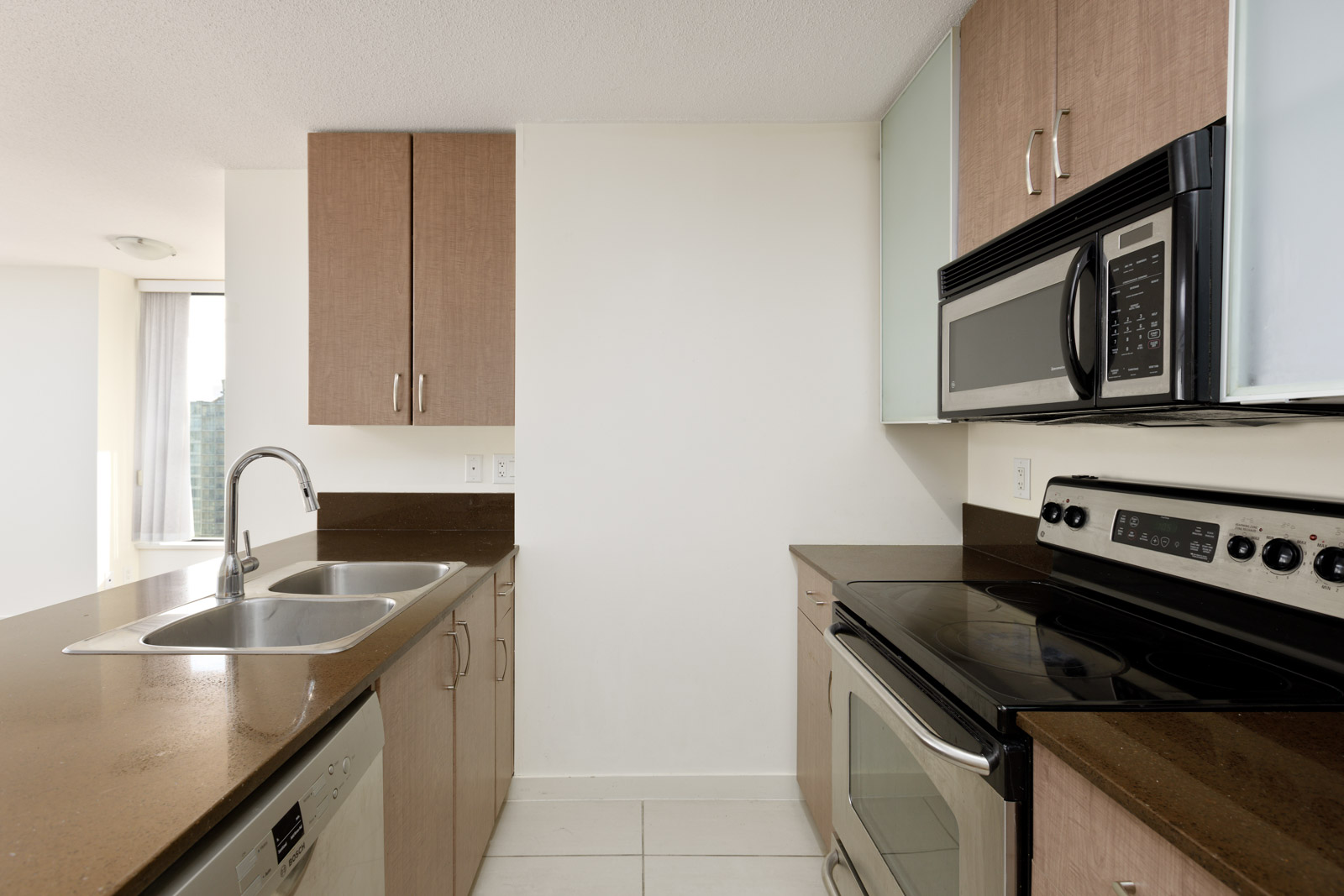 Modern kitchen with brown countertops, stainless steel appliances, a double sink, electric stove, microwave, and light brown cabinets.