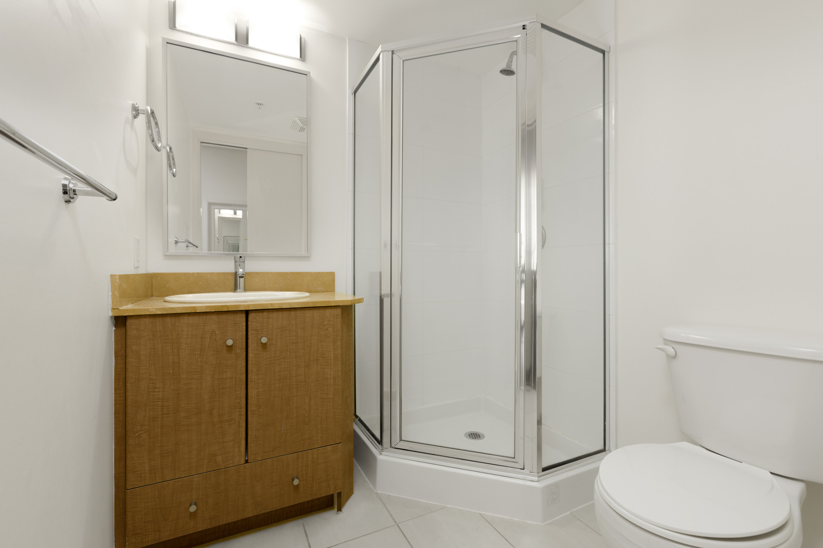 A bathroom with a wooden vanity and sink, a glass-enclosed corner shower, a toilet, and white walls.