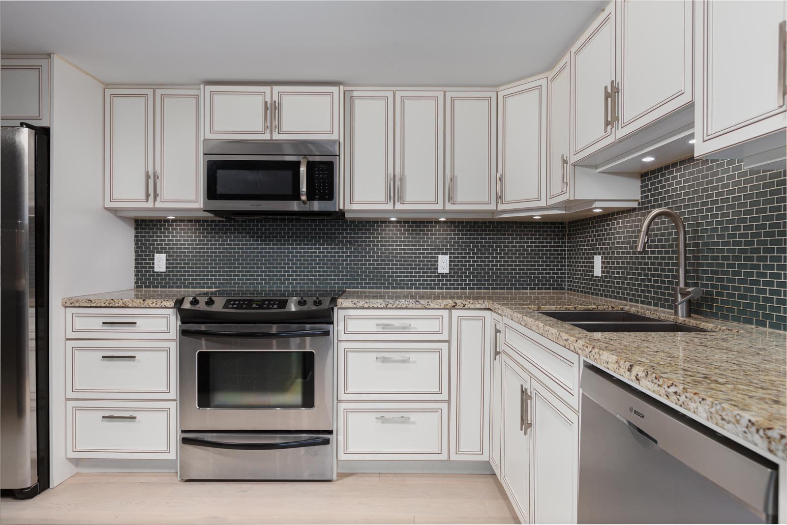 Modern kitchen with white cabinets, stainless steel appliances, granite countertops, and a dark tile backsplash.