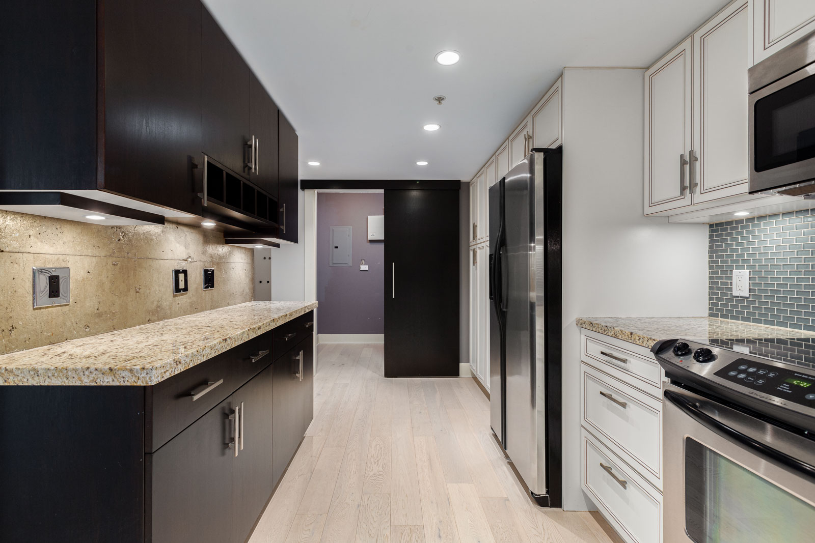 Modern kitchen with granite countertops, stainless steel appliances, dark and light cabinetry, light wood flooring, and recessed ceiling lights.