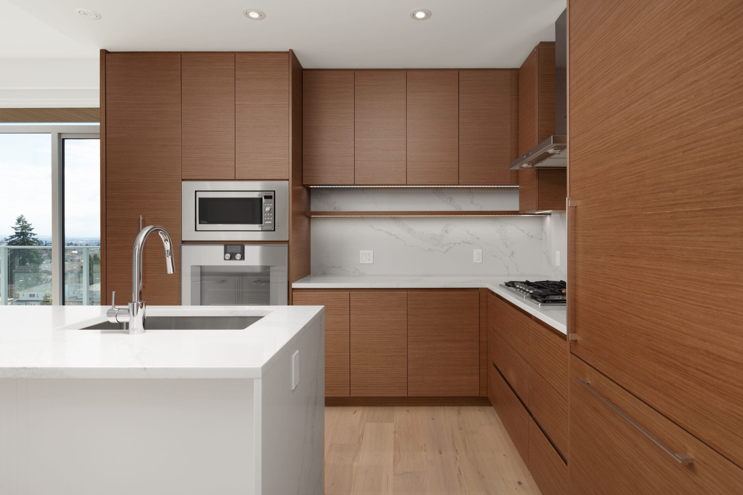 Modern kitchen with wood cabinets, white countertops, built-in microwave, induction stove, and large window providing natural light.