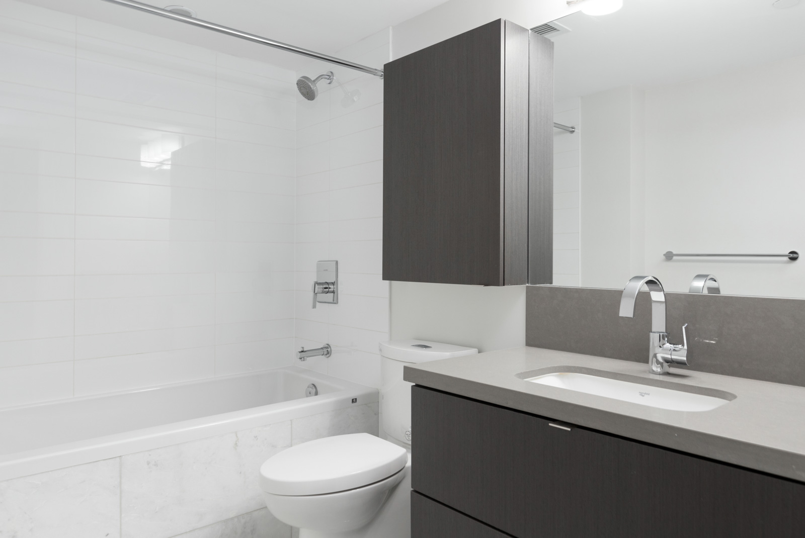 Modern bathroom with a bathtub-shower combo, toilet, dark wood vanity with sink, and a large mirror above the sink.