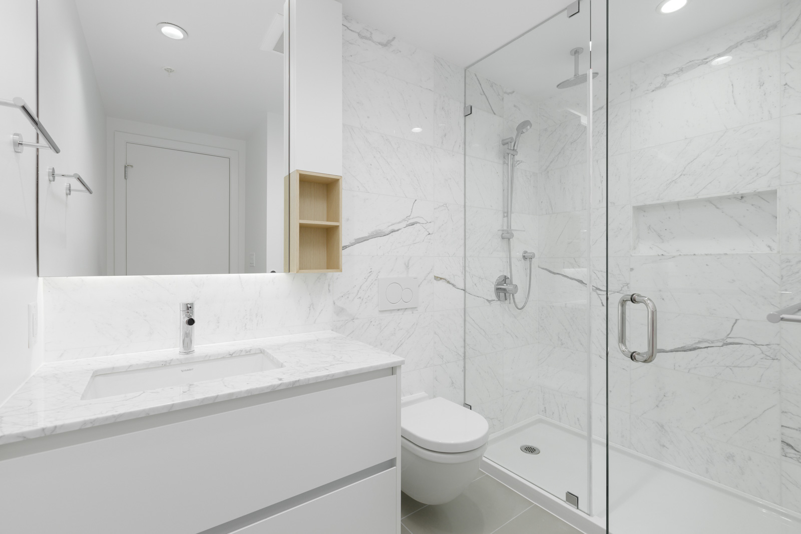Minimalist white bathroom with marble surfaces, glass-enclosed shower, wall-mounted toilet, and a vanity with a rectangular sink and mirror.