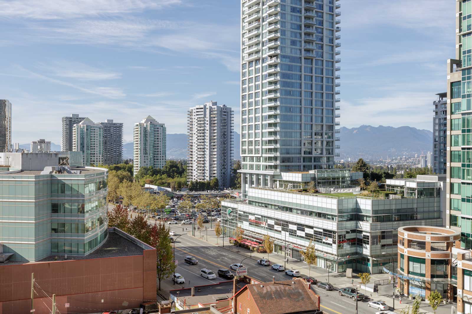 High-rise buildings and office towers line a busy urban street with cars; distant mountains are visible under a clear sky.