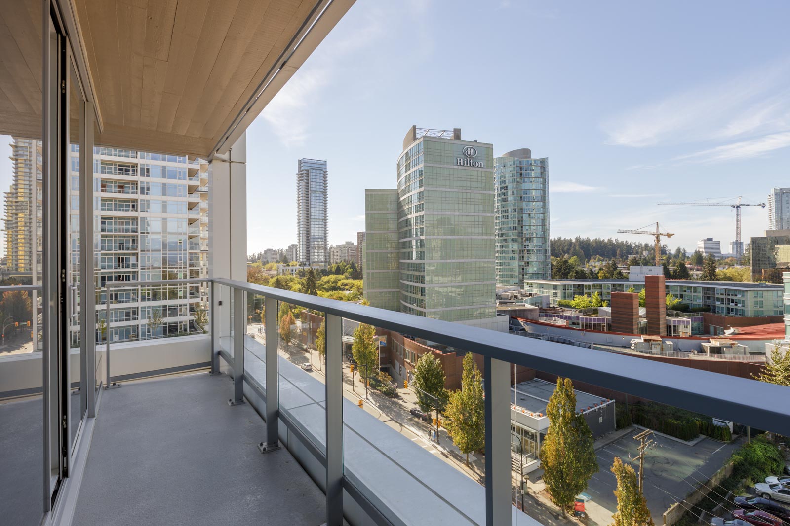 View from a balcony overlooking modern office buildings, including a Hilton hotel, with trees and a cityscape in the background on a clear day.